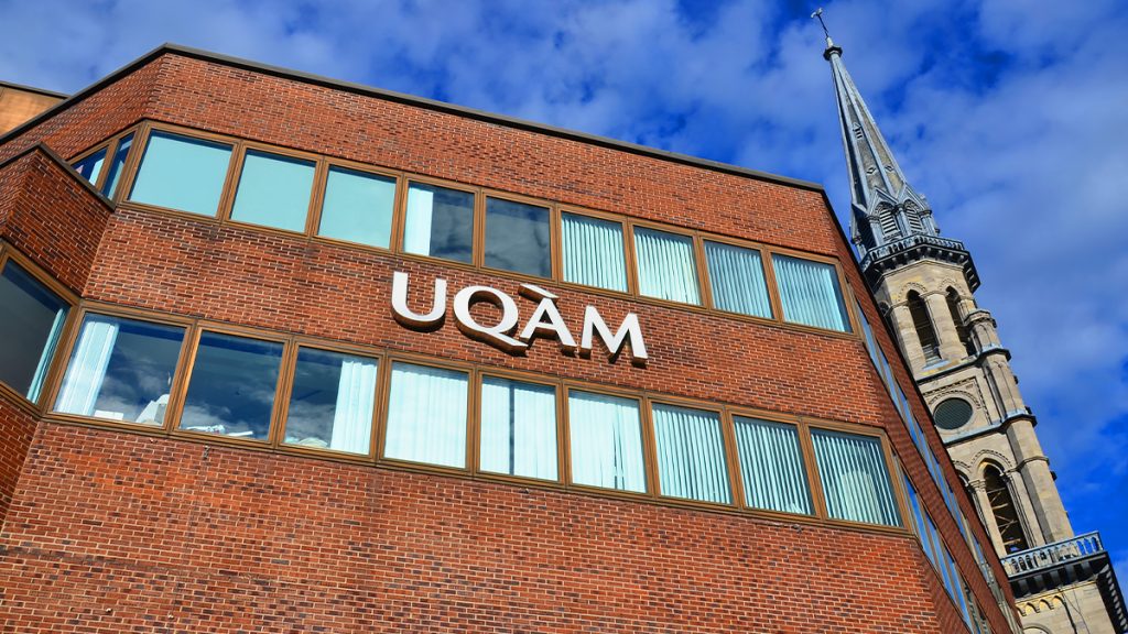 Photo en contre plongée, d'un pavillon en briques rouge. On y voit le logo de l'UQAM posé sur la façade entre deux rangées de fenêtres.